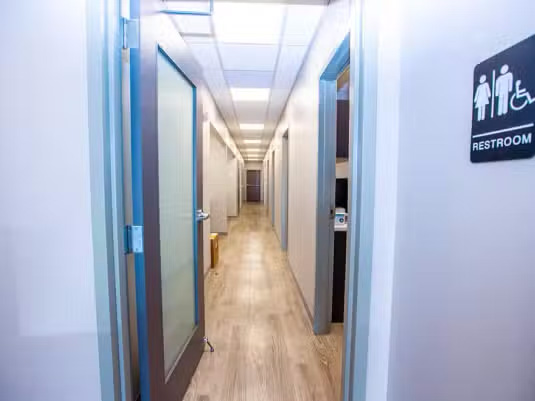 The image shows a long hallway with doors on either side, leading to restrooms, and there s a sign indicating a gender-neutral restroom.