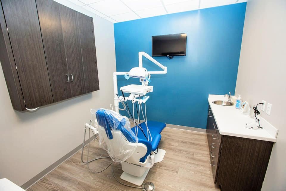 The image shows a dental office interior with a dental chair, a countertop with a sink, cabinets, and a TV screen.