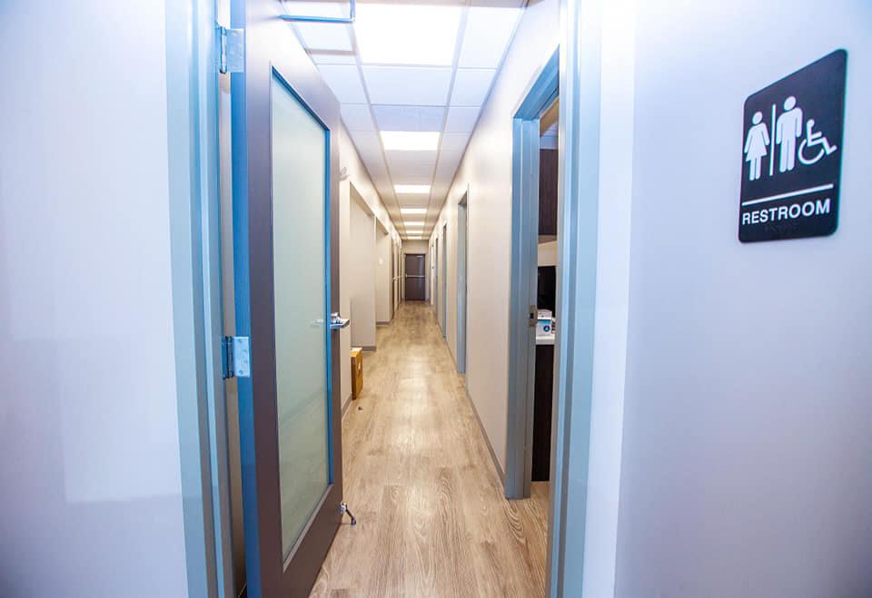 The image shows an interior hallway with a sign indicating a restroom on the right side, and there s an open door leading into another room.