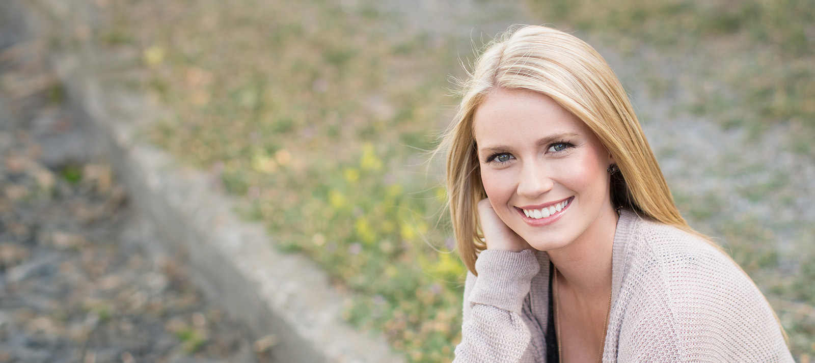 Young woman with blonde hair posing outdoors, smiling at the camera.