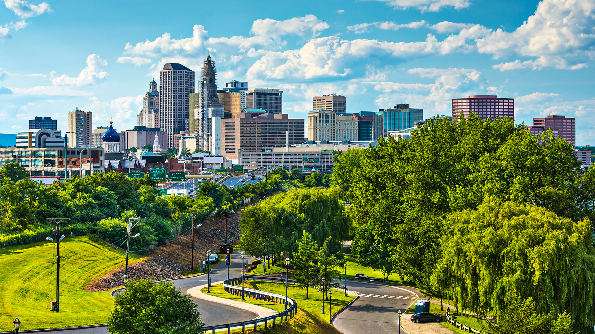 A city skyline with a clear sky and lush green trees in the foreground.