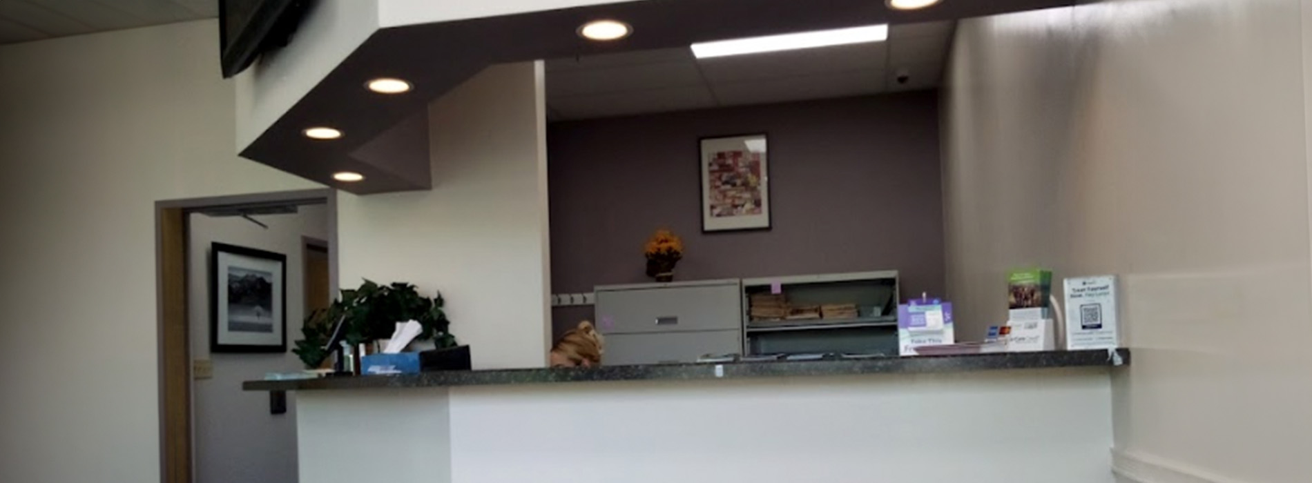 The image depicts a reception area with a counter and a sign above it, taken from an angle that makes the space appear distorted due to the camera s perspective.