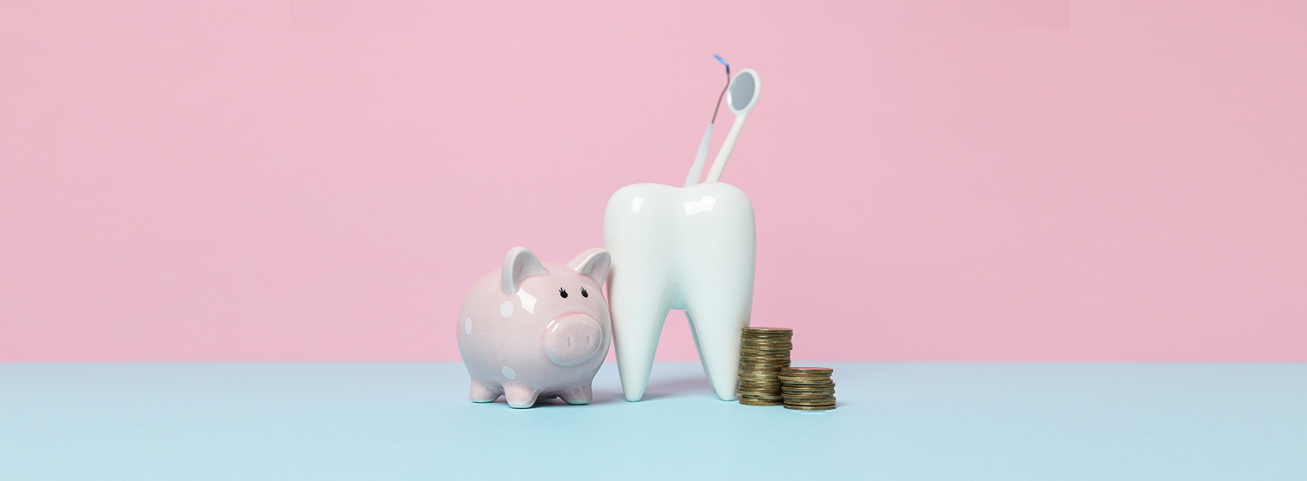 The image shows a small pink piggy bank with coins inside, placed on a light blue surface, next to a white toothbrush holder containing a toothbrush, against a backdrop of a plain pink wall.