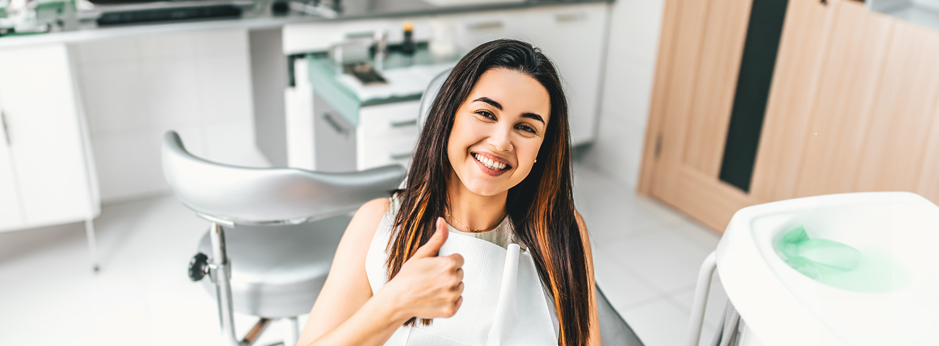 A woman sitting at a dental chair, smiling towards the camera, with a cup of coffee on the table next to her.