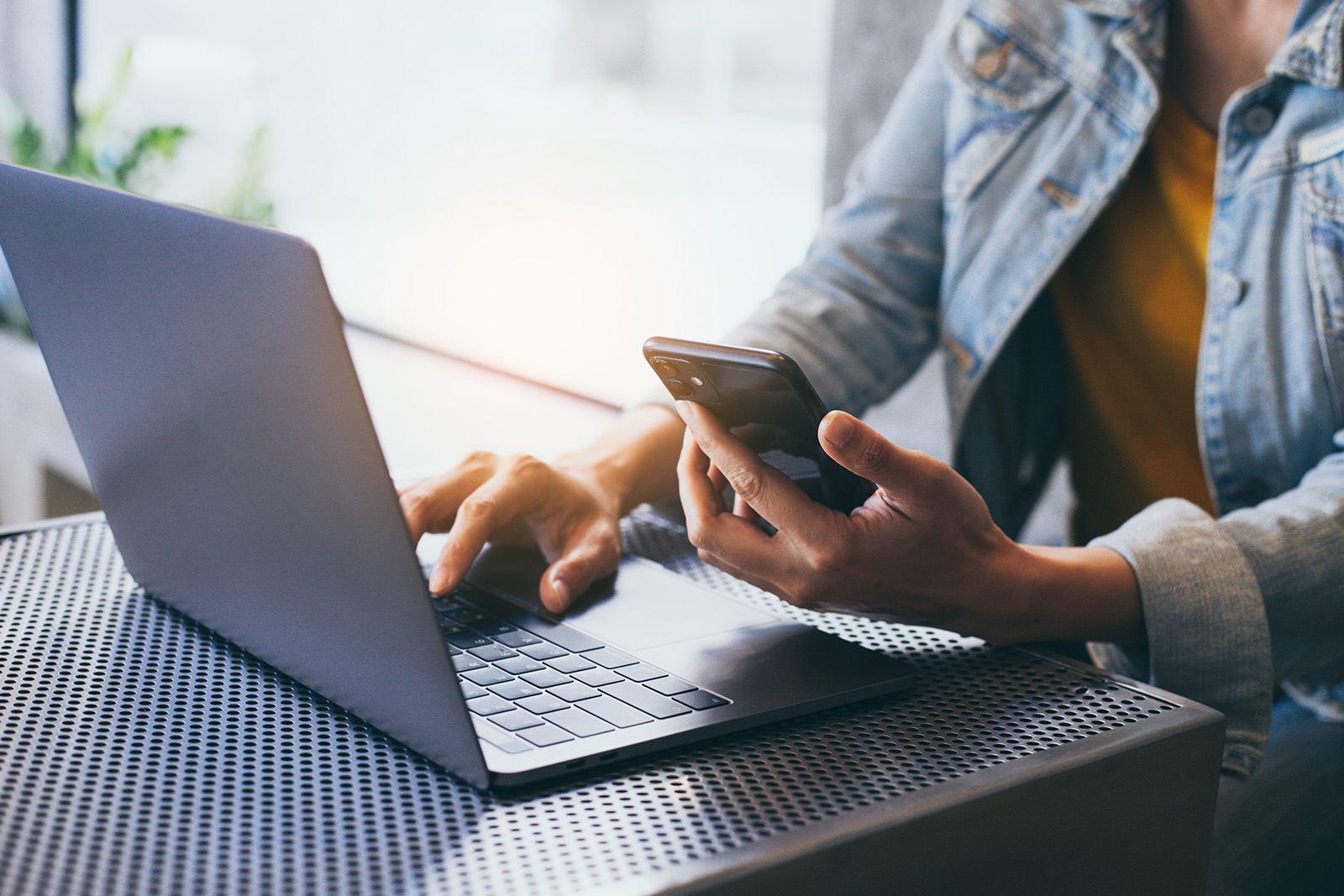 A person using a laptop while seated at a table with their hands on a keyboard.