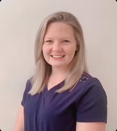 A woman wearing a white lab coat over a blue shirt, posing with a slight smile against a neutral background.