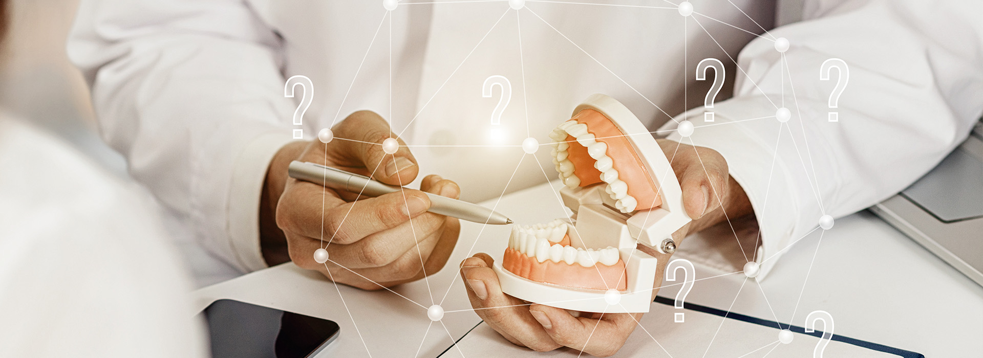 The image shows a person s hand holding a dental model with teeth, while another person appears to be working on a computer screen displaying digital information relevant to dentistry, possibly related to patient data or treatment planning.