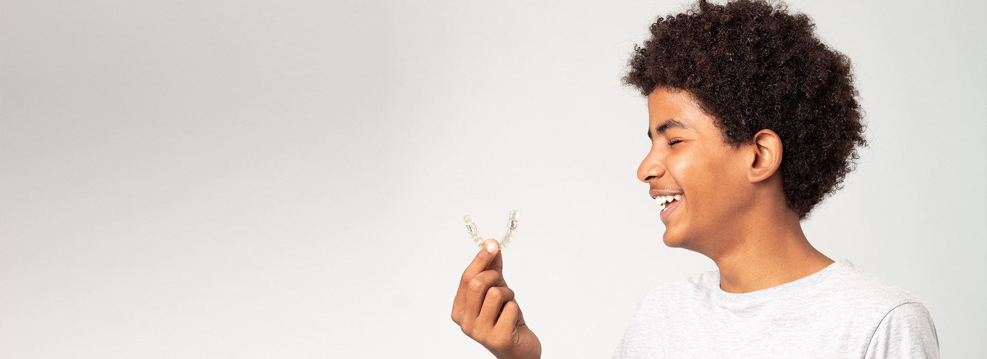 The image displays a person holding a small white object with a smile on their face, against a neutral background.