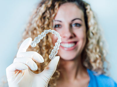 A woman wearing a surgical mask holds up a dental implant with a smile.