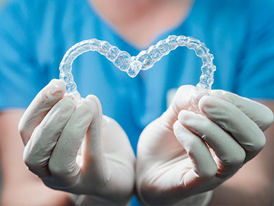 An individual wearing medical gloves holds up a heart-shaped dental implant.