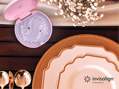 The image shows a collection of tableware including plates, bowls, and spoons arranged on a wooden surface with a pink box containing dental implant components in the foreground.