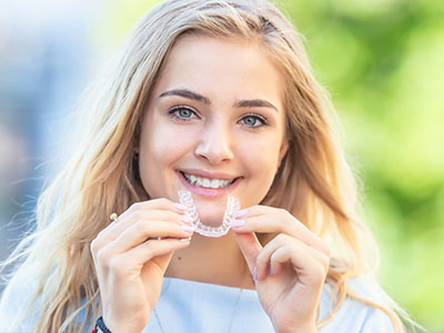 A young woman smiling at the camera while holding a toothbrush with bristles.