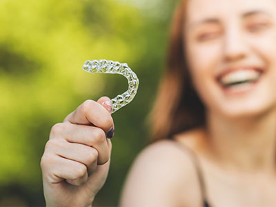 An adult woman with a radiant smile holds up a white plastic dental retainer.