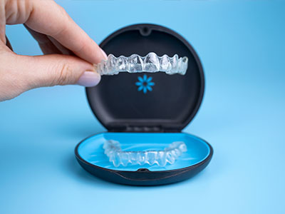 An open package of transparent dental aligners displayed against a blue background.