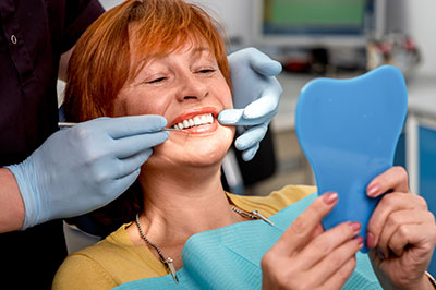 A woman sitting in a dental chair with a smile on her face, receiving dental care from a professional who is adjusting her teeth with tools.