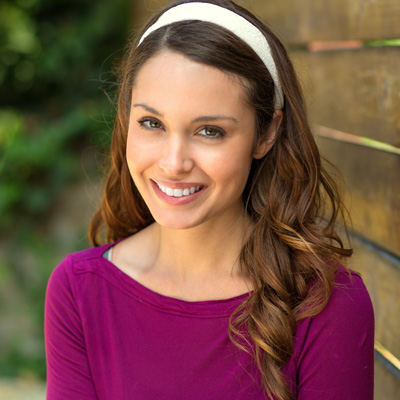 A woman with long hair wearing a purple top and headband smiles at the camera.