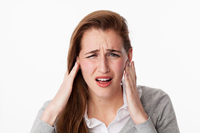 The image shows a woman with her hand on her head, appearing to be experiencing discomfort or pain, possibly due to stress or illness.