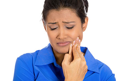 A woman with her eyes closed, holding a toothbrush near her mouth, appears to be brushing her teeth.