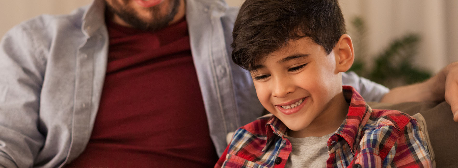 A man and a young boy are sitting together on a couch, smiling at each other.