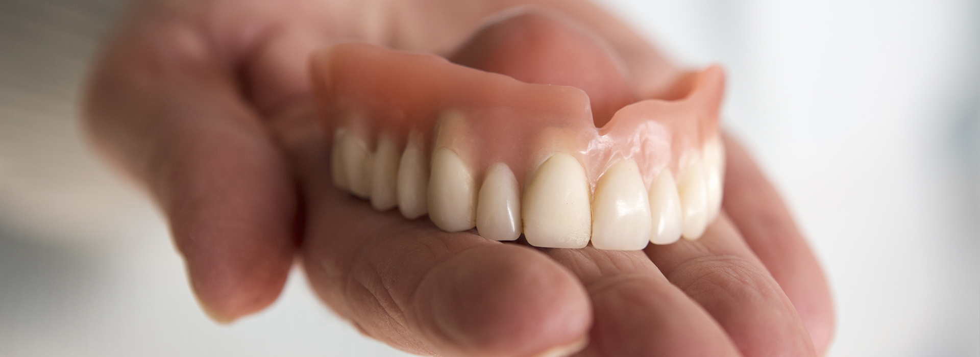 A person holding a set of dentures with their left hand.