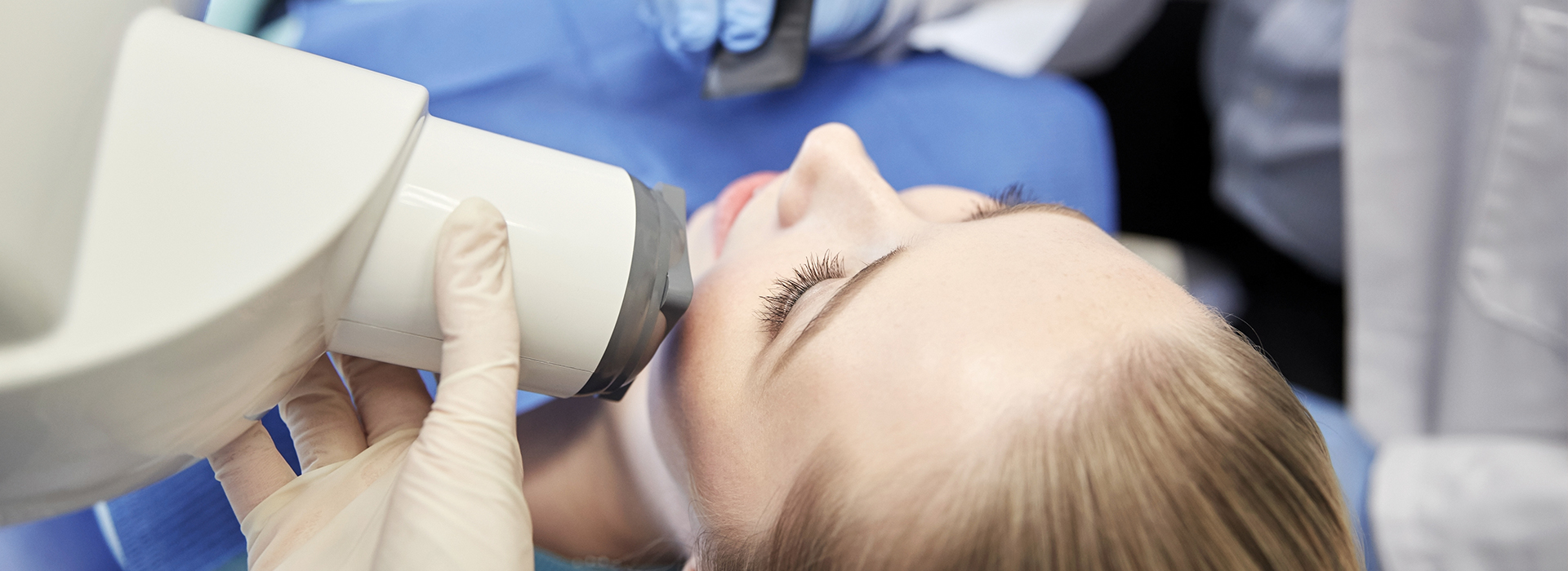 The image shows a person receiving dental care with a dentist using a magnifying device to examine their teeth closely.