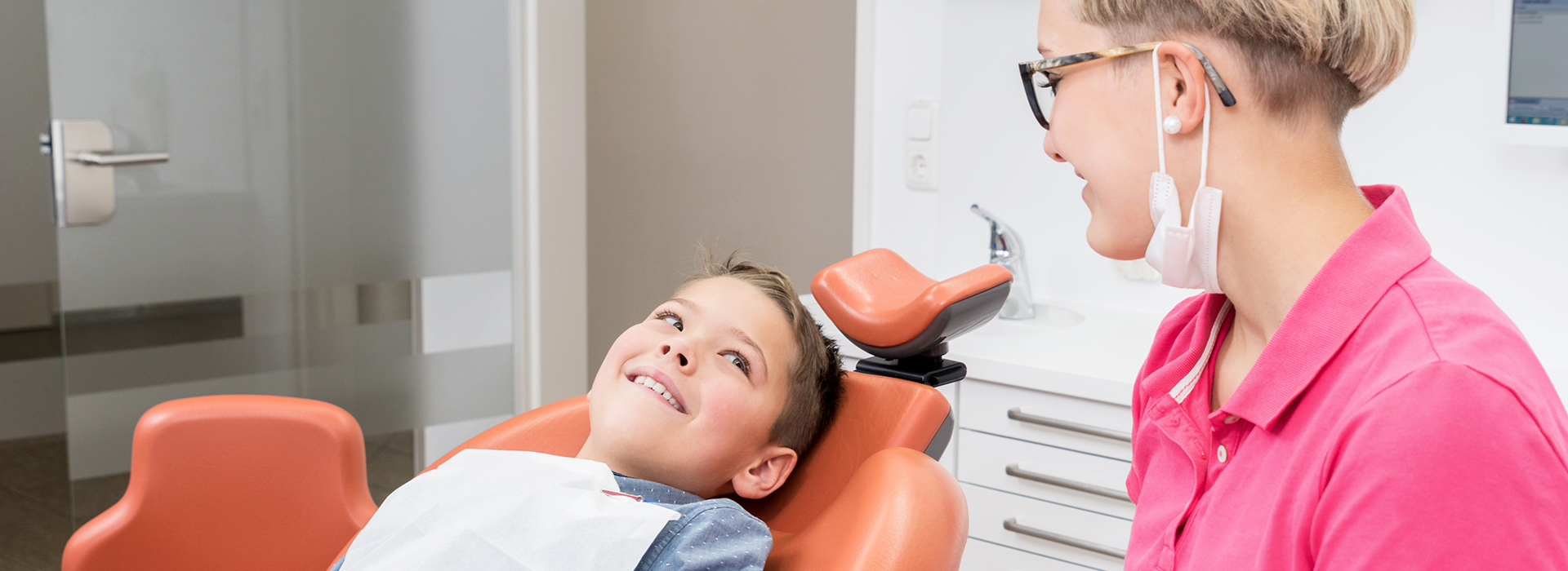 A young child sitting in a dental chair with a dentist, receiving dental care.