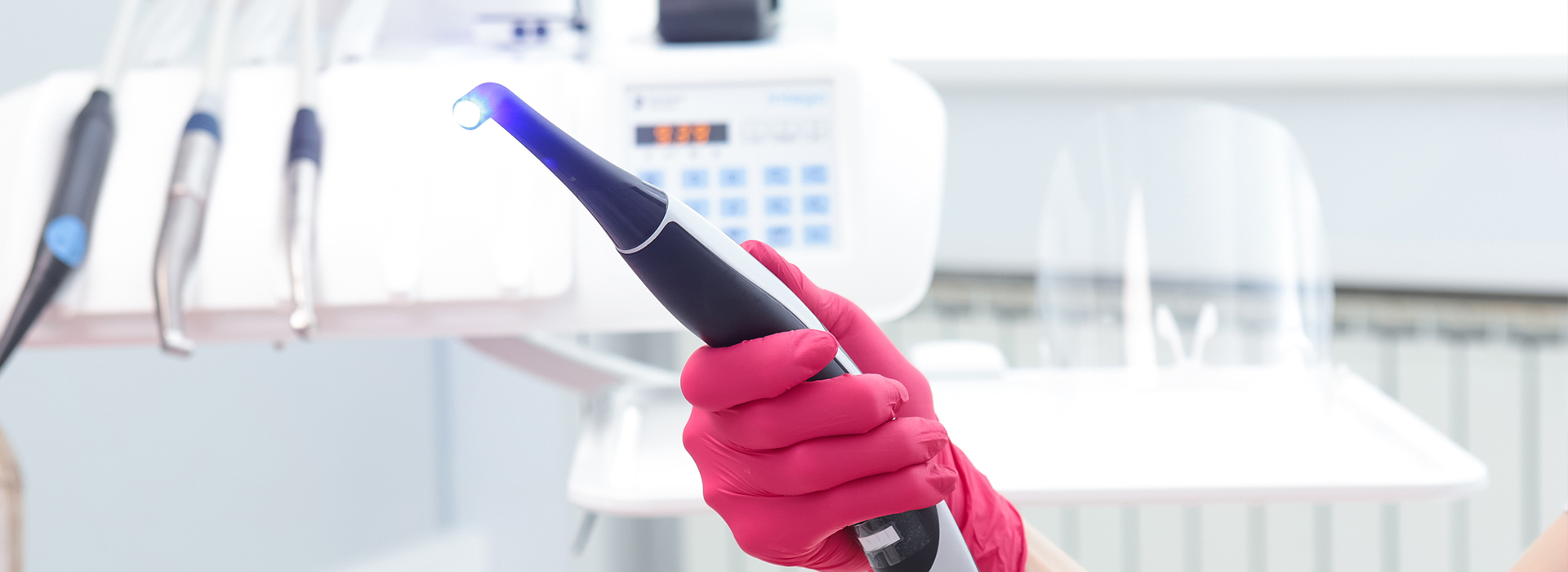 The image shows a person holding an object with a blue light, wearing protective gloves and standing in front of a counter with medical equipment.