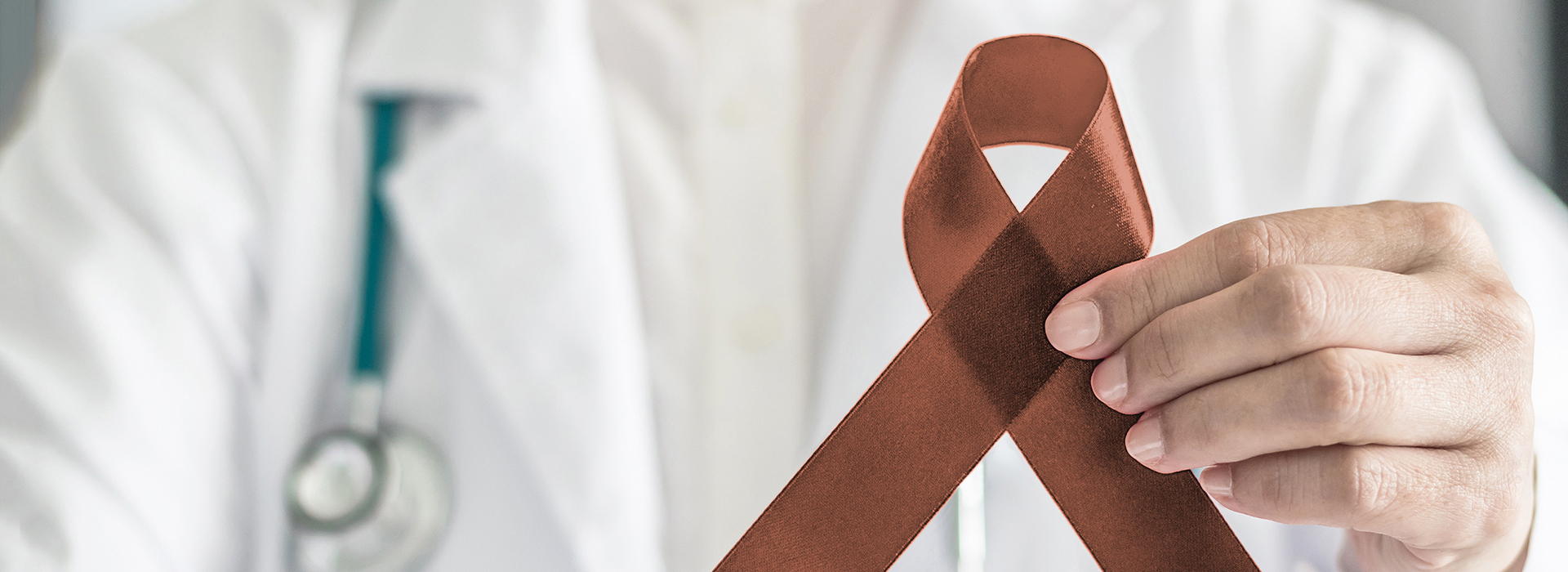 The image shows a healthcare professional holding up a red ribbon with a white cross symbolizing medical aid, against a medical background.