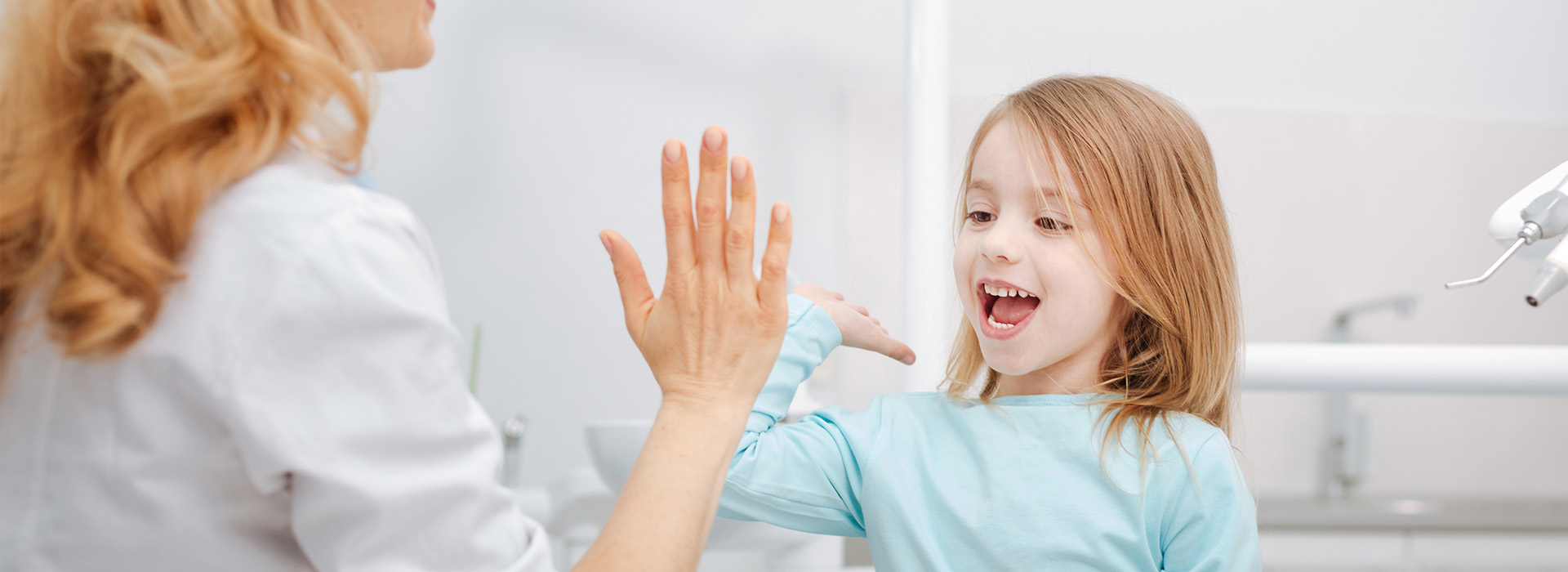 A young girl with blonde hair receiving a high five from an adult female, both in a bathroom setting.