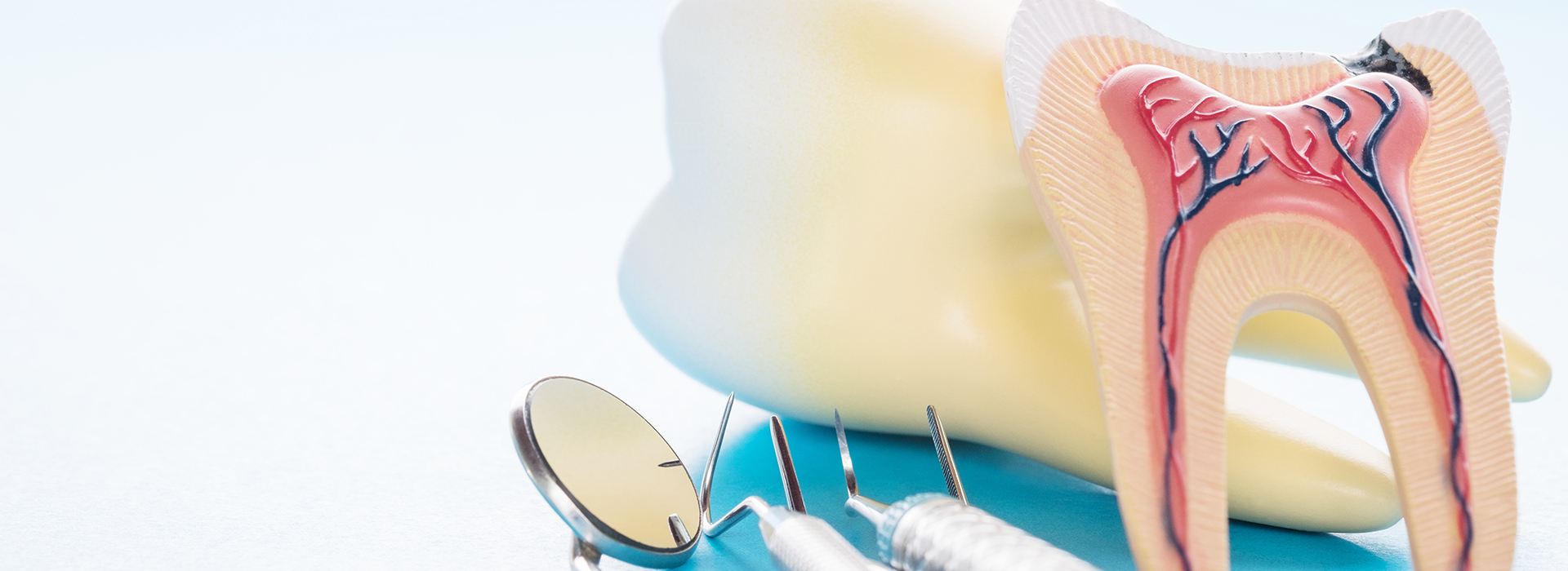 The image shows a close-up of a dental model with a toothbrush and dental floss, accompanied by a tongue depressor with an illustration of a mouth on it, all set against a blurred background that appears to be a blue sky.