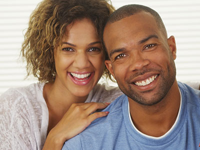 A man and woman smiling at the camera, with the man wearing a dark-colored t-shirt and the woman in a white top.