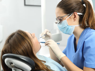 A dental hygienist working on a patient s teeth with tools visible.