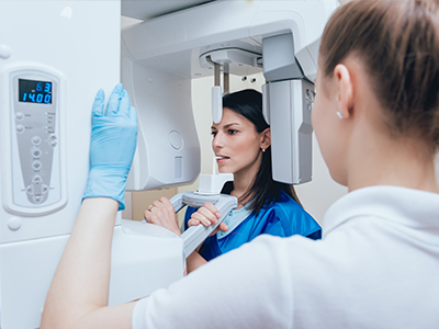 A woman in blue scrubs stands next to a large 3D scanner with a digital display, while another woman in white observes the equipment.