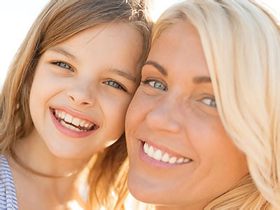 The image shows a woman and a young girl smiling at each other, with the woman s face partially obscured by the camera angle.