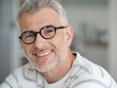 A middle-aged man with gray hair, wearing glasses and a white shirt, smiling at the camera.