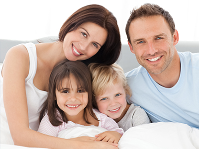 A family of four adults and two children posing together on a bed with a smiling expression.