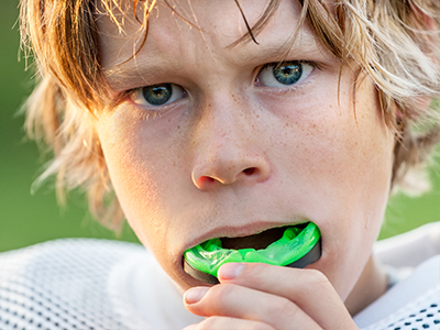 The image shows a young person with blonde hair and a concerned expression, holding a green object close to their mouth.